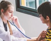 A school nurse uses a stethoscope to check a young student’s heart rate.