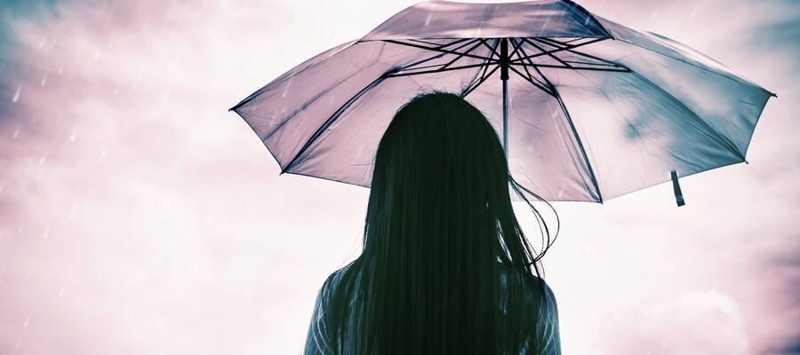 A woman standing with her back to the camera holding an umbrella and looking out to a cloudy sky.