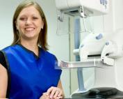 A female radiologic technologist stands beside medical equipment