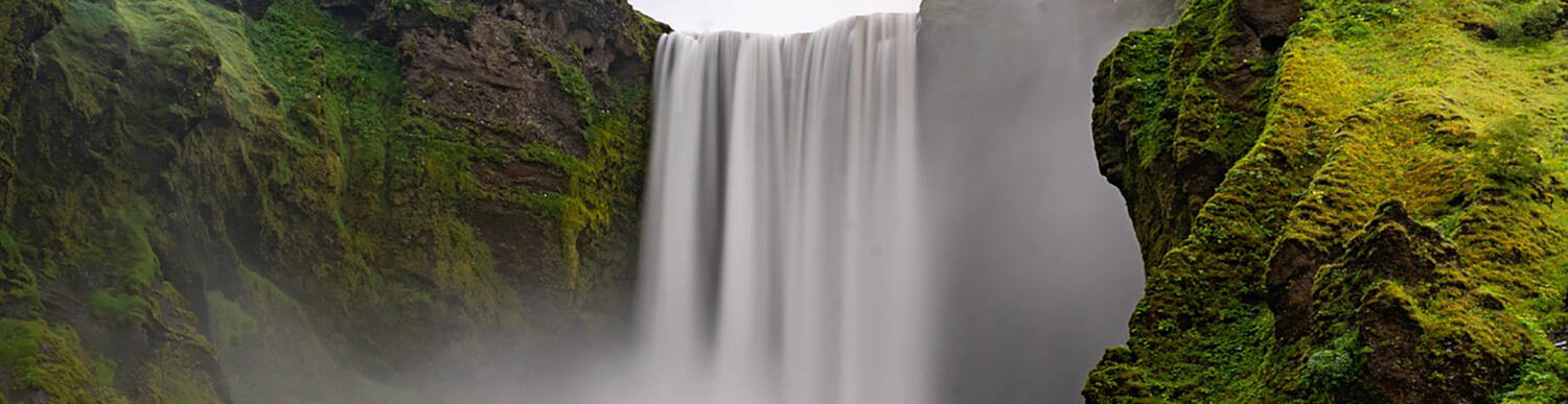 A water fall surrounded by greenery in a mountain area.