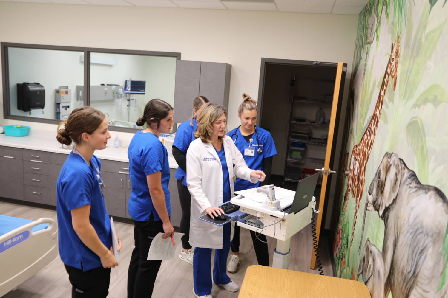 Four Marian University nursing students and a nursing instructor in the pediatric learning simulator all surrounding a computer.