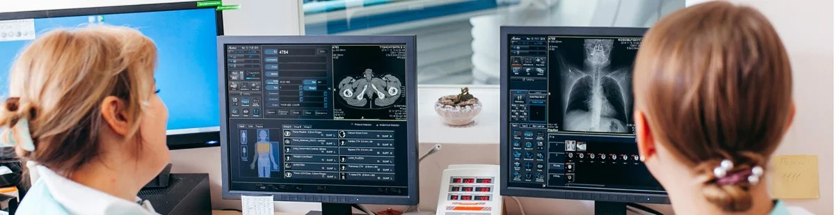 Two healthcare professionals analyzing radiologic information on computers in an office.